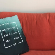 Wide image with a red couch and a pillow which says "The mountains are calling I must go"